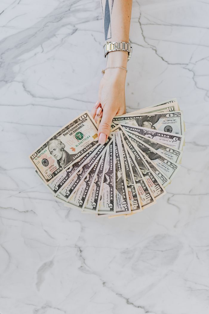 A hand with wristwatch holding a fan of US dollar bills on a marble surface, symbolizing wealth and financial abundance.